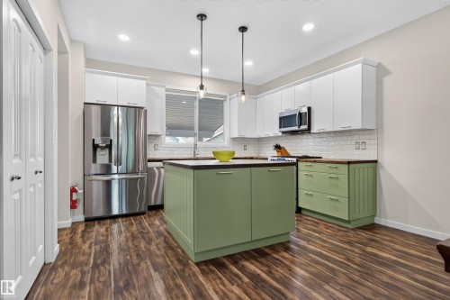 Contemporary kitchen featuring a central island with green cabinetry, wood-finish flooring, and white upper cabinets - 6928 22 Avenue, Edmonton, AB 