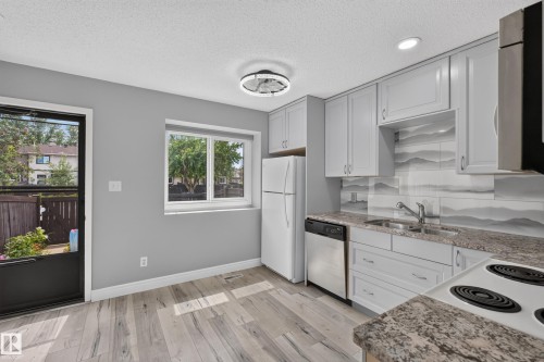Modern kitchen featuring light gray cabinetry, a decorative tile backsplash, and wood-finish flooring - 178 Tudor Lane, Edmonton, AB 