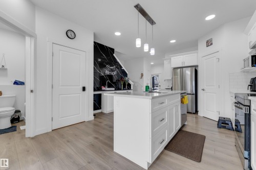 Modern kitchen featuring a central island with countertop seating, white shaker cabinetry, stainless steel appliances, and wood-finish flooring - 432 29 Street, Edmonton, AB 