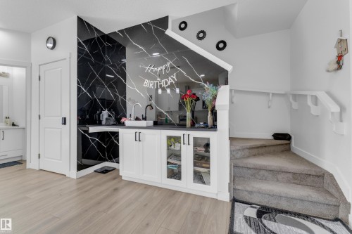 Integrated wet bar featuring a black marble-patterned backsplash, white cabinetry with glass inserts, a single basin sink, and a dark countertop - 432 29 Street, Edmonton, AB 