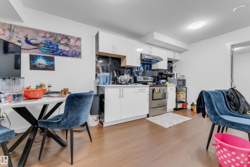 Modern kitchen featuring white cabinetry, stainless steel appliances, dark stone-finish backsplash, and wood-finish flooring - 432 29 Street, Edmonton, AB 