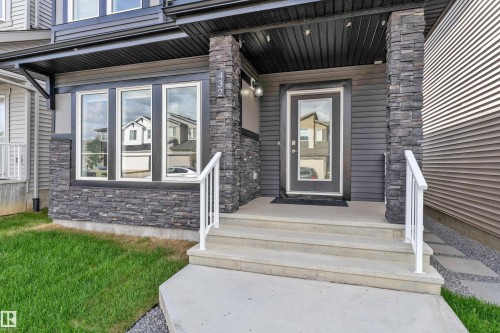 Modern exterior featuring dark siding, stone veneer accents, concrete steps with white railings, and a glass-paneled entry door - 432 29 Street, Edmonton, AB 
