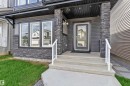 Modern exterior featuring dark siding, stone veneer accents, concrete steps with white railings, and a glass-paneled entry door - 432 29 Street, Edmonton, AB 
