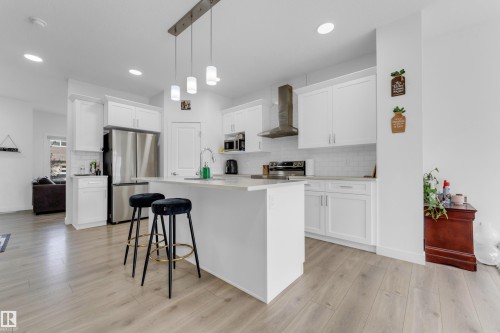 Modern kitchen featuring white shaker cabinetry, stainless steel appliances, a center island with sink, subway tile backsplash, and light wood-finish flooring - 432 29 Street, Edmonton, AB 