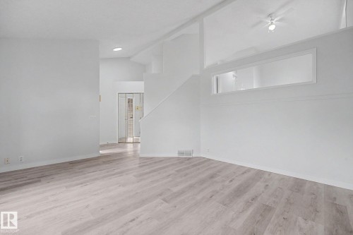 Spacious room featuring light wood-finish flooring, white walls, and a high ceiling with a ceiling fan - 3704 39 Avenue, Edmonton, AB 