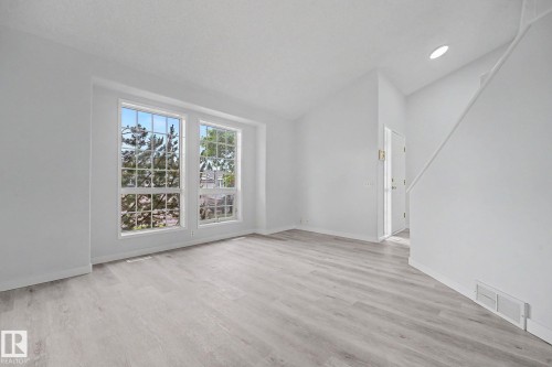 Spacious room featuring light wood-finish flooring, crisp white walls, and two large multi-pane windows - 3704 39 Avenue, Edmonton, AB 