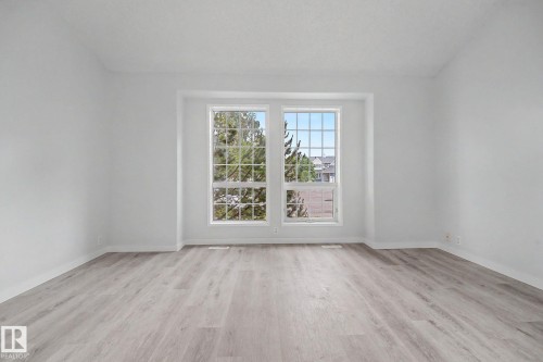 Spacious room featuring light wood-finish flooring, white baseboards, and a large window with grid panes - 3704 39 Avenue, Edmonton, AB 