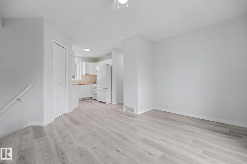Open-concept living area with light wood-finish flooring, white walls, a ceiling fan, and staircase with white railing - 3704 39 Avenue, Edmonton, AB 