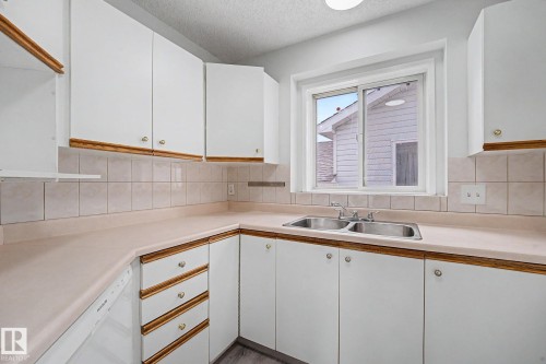 Bright kitchen featuring white cabinetry with wood-finish trim, a double basin stainless steel sink, beige countertops, and a tiled backsplash - 3704 39 Avenue, Edmonton, AB 