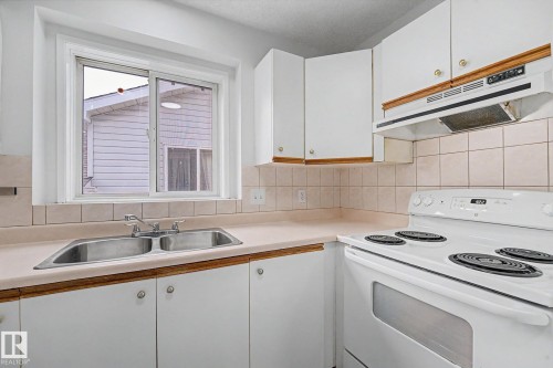 Kitchen featuring white cabinetry, a double basin stainless steel sink, a tile backsplash, light-toned countertops, and a white electric range with an overhead vent - 3704 39 Avenue, Edmonton, AB 