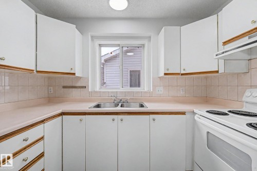 Kitchen featuring white cabinetry with wood trim accents, a double basin stainless steel sink, a tile backsplash, light-toned countertops, and a white electric range - 3704 39 Avenue, Edmonton, AB 