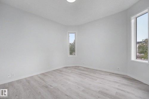 Bright room featuring light wood-finish flooring, white baseboards, and two windows providing natural light - 3704 39 Avenue, Edmonton, AB 