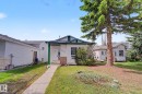Front exterior with white siding and green trim, featuring a concrete walkway, a small porch, and a large mature evergreen tree - 3704 39 Avenue, Edmonton, AB 