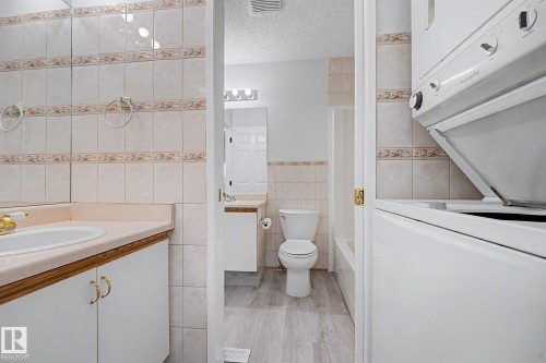 Bathroom featuring a vanity with an integrated sink, large wall-mounted mirror, and tile wainscoting - 3704 39 Avenue, Edmonton, AB 