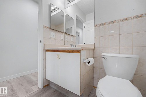 Bathroom featuring a built-in vanity with white cabinetry, a ceramic tile backsplash, dual wall-mounted mirrors, and light wood-finish flooring - 3704 39 Avenue, Edmonton, AB 