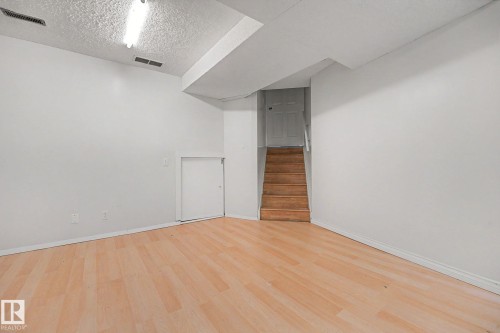 Spacious room featuring light wood-finish flooring, white walls, and a dropped ceiling - 3704 39 Avenue, Edmonton, AB 