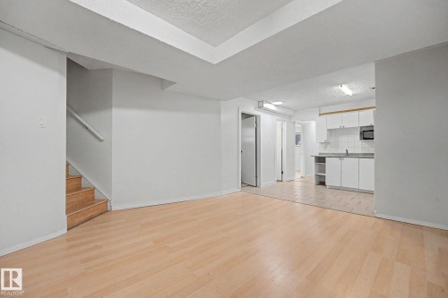 Open concept living area with wood-finish flooring, white walls, and stairs featuring a wooden handrail - 3704 39 Avenue, Edmonton, AB 