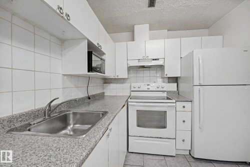 Kitchen featuring white cabinetry, a built-in stainless steel sink, and a white tile backsplash - 3704 39 Avenue, Edmonton, AB 