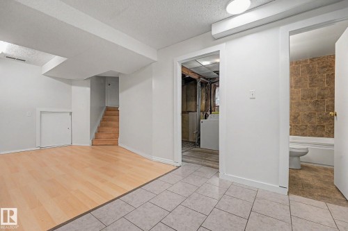 Lower level featuring a tiled entry, wood-finish flooring, a wooden staircase, and access to a bathroom with a tiled shower surround - 3704 39 Avenue, Edmonton, AB 