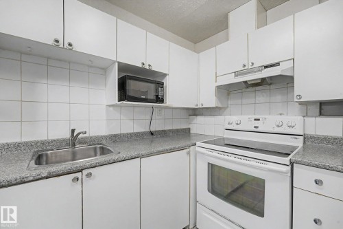 Compact kitchen featuring white cabinetry, a stainless steel sink, speckled countertops, a white electric range, and a built-in microwave shelf - 3704 39 Avenue, Edmonton, AB 