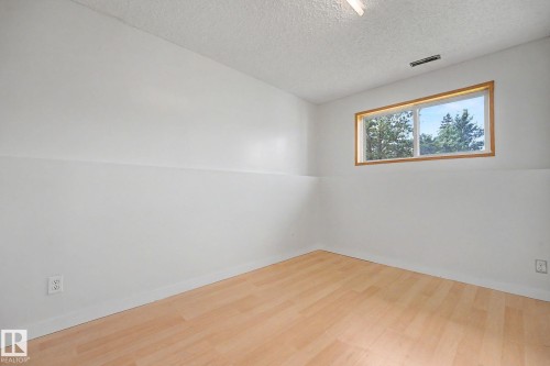 Room featuring a horizontal window with wood trim, light wood-finish flooring, white painted walls, and a textured ceiling - 3704 39 Avenue, Edmonton, AB 