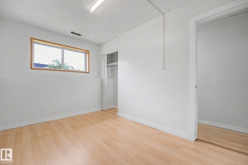Bright room featuring wood-finish flooring, a wood-framed window, a built-in closet with bifold doors, and a mirrored sliding door - 3704 39 Avenue, Edmonton, AB 