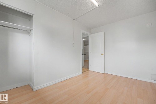 Bright room featuring light wood-finish flooring, white walls, and a built-in closet with shelving and hanging rod - 3704 39 Avenue, Edmonton, AB 