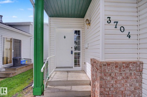 Front entry featuring a paneled door with sidelight, concrete steps, and white railing - 3704 39 Avenue, Edmonton, AB 