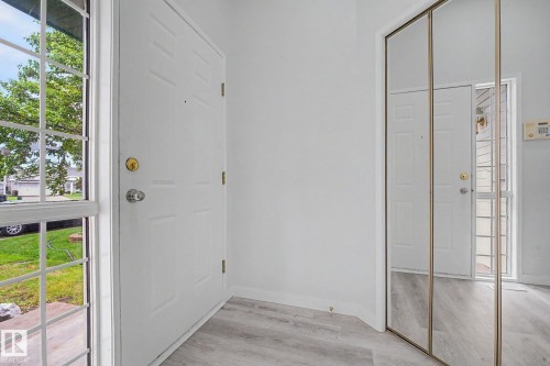 Entryway featuring light wood-finish flooring, a white paneled front door, and a mirrored closet door with a gold-tone frame - 3704 39 Avenue, Edmonton, AB 