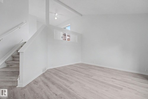 Spacious interior featuring light wood-finish flooring, white walls, and an open stairwell with a white railing - 3704 39 Avenue, Edmonton, AB 