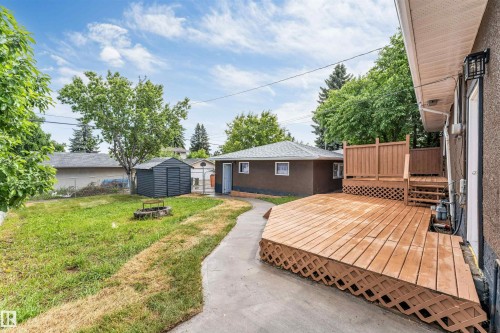 Spacious backyard featuring a multi-level wood deck with lattice skirting, concrete path, and a storage shed - 6404 88 Avenue, Edmonton, AB 