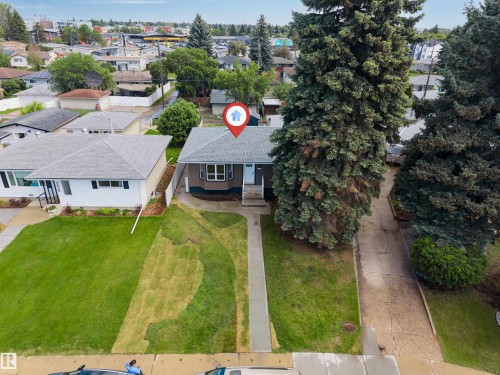 Single-story residence with a gray shingled roof and brown siding, featuring a front lawn and mature evergreen trees - 6404 88 Avenue, Edmonton, AB 
