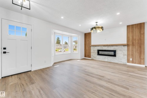 Living area featuring wood-finish flooring, a contemporary fireplace with a stone surround, and wood paneling accents - 6404 88 Avenue, Edmonton, AB 