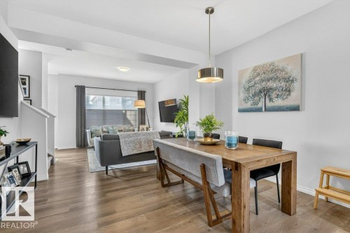 Open-concept living and dining areas featuring wood-finish flooring, a contemporary dining pendant light, recessed lighting, and a large window with blinds - 3708 42 Avenue, Beaumont, AB 