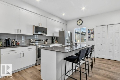Contemporary kitchen featuring white cabinetry, stainless steel appliances, a center island with bar seating, and wood-finish flooring - 3708 42 Avenue, Beaumont, AB 