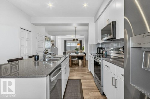 Kitchen featuring a large island with an undermount double-basin sink, stainless steel appliances, white cabinetry, and gray countertops - 3708 42 Avenue, Beaumont, AB 