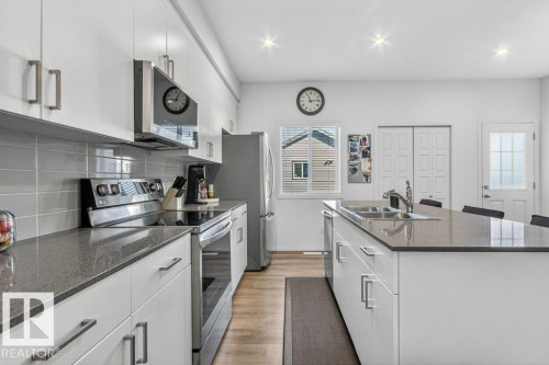 Modern kitchen featuring white cabinetry, dark countertops, a stainless steel appliance suite, wood-finish flooring, and recessed lighting - 3708 42 Avenue, Beaumont, AB 