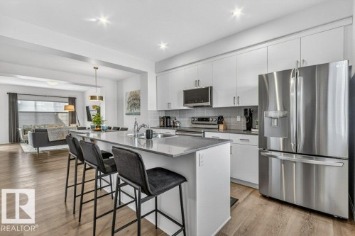 Modern kitchen featuring an island with seating, stainless steel appliances, white cabinetry, and wood-finish flooring - 3708 42 Avenue, Beaumont, AB 