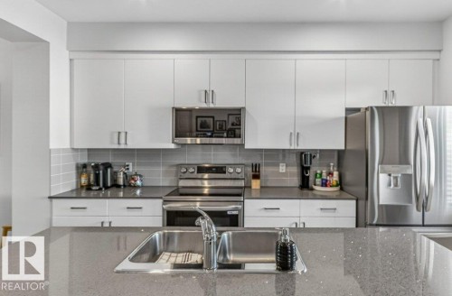 Kitchen featuring white shaker-style cabinetry, stainless steel appliances, a grey subway tile backsplash, and dark countertops - 3708 42 Avenue, Beaumont, AB 