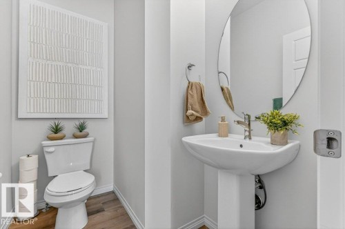 Pedestal sink with chrome faucet, oval wall-mounted mirror, and wood-finish flooring - 3708 42 Avenue, Beaumont, AB 