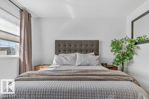 Bedroom featuring a tufted upholstered headboard, window with blinds and drapes, and white wall finishes - 3708 42 Avenue, Beaumont, AB 