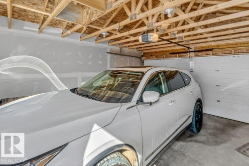 Attached garage featuring unfinished exposed wood ceiling trusses, a concrete floor, and white panel garage doors - 3708 42 Avenue, Beaumont, AB 