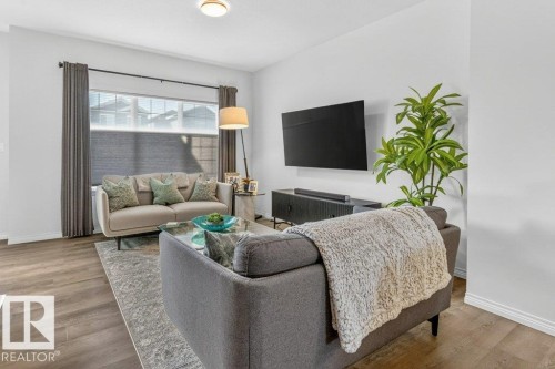 Living area featuring wood-finish flooring, white baseboards, and a large window with privacy blinds and drapes - 3708 42 Avenue, Beaumont, AB 