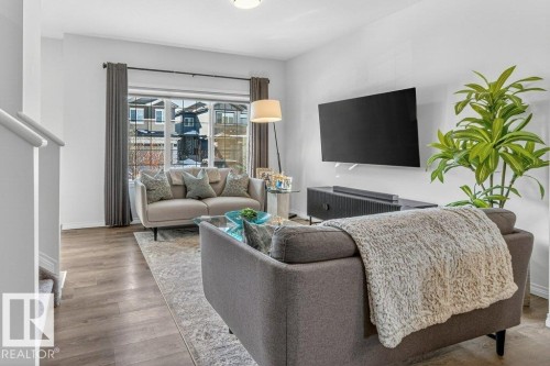 Bright living area featuring wood-finish flooring, a large bay window with dark drapery, and a white stair railing - 3708 42 Avenue, Beaumont, AB 