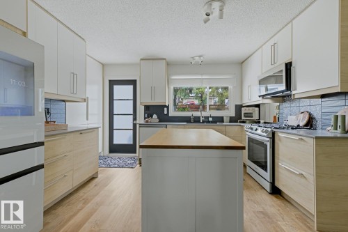Contemporary kitchen featuring an island with a butcher block countertop, wood-finish flooring, two-tone cabinetry, stainless steel appliances, and a tiled backsplash - 3504 102 Avenue, Edmonton, AB 