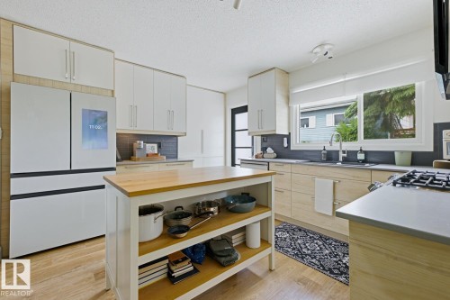 Well-appointed kitchen featuring a substantial central island with wood countertop, modern white upper cabinetry, and light wood-finish lower cabinetry - 3504 102 Avenue, Edmonton, AB 