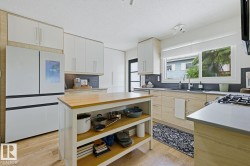 Well-appointed kitchen featuring a substantial central island with wood countertop, modern white upper cabinetry, and light wood-finish lower cabinetry - 