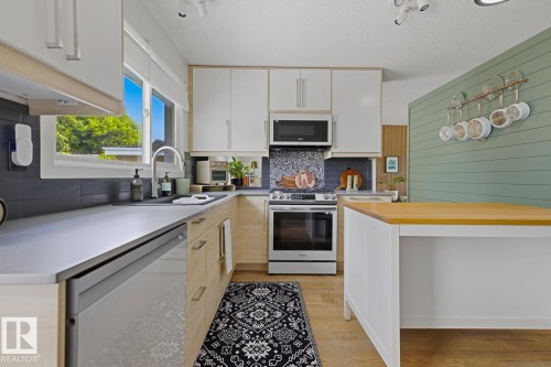 Modern kitchen featuring light wood-finish lower cabinetry, white upper cabinetry, and stainless steel appliances including an oven range, microwave, and dishwasher - 3504 102 Avenue, Edmonton, AB 