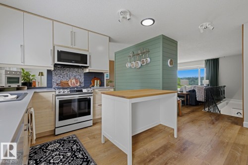 Modern kitchen featuring light wood-finish lower cabinetry, white upper cabinetry, and stainless steel appliances - 3504 102 Avenue, Edmonton, AB 