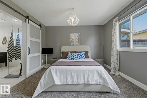 Grey-painted room featuring a contemporary light fixture, a large window with white framing, and wall-to-wall carpeting - 3504 102 Avenue, Edmonton, AB 